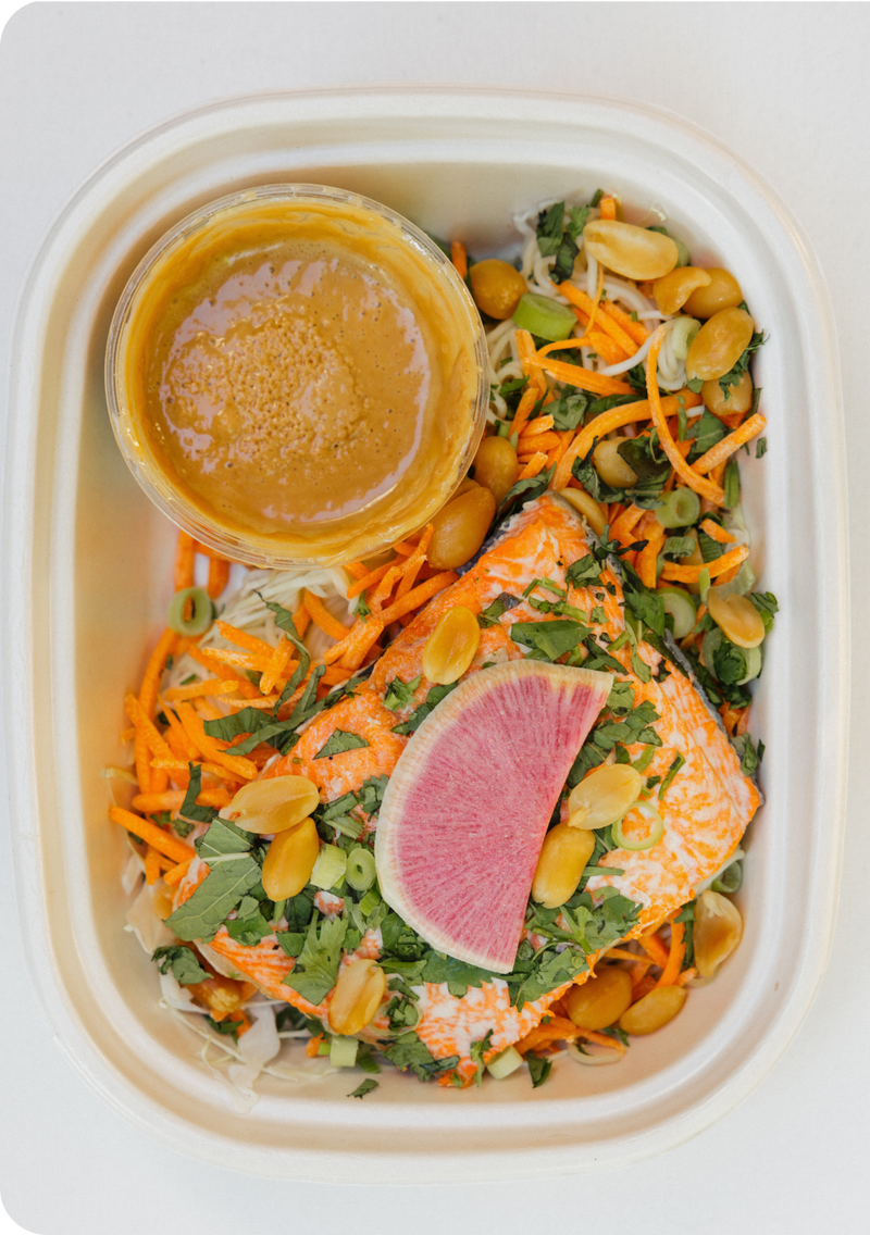 Salad with oranges, carrots, and a dressing in a white container on a white background